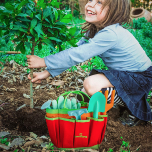 Girl digging in a garden next to a canvas garden tool bag to celebrate earth day