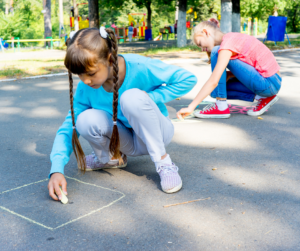 Two kids outside drawing with sidewalk chalk