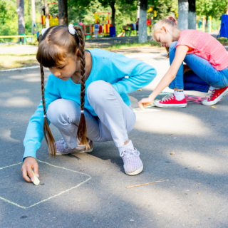Two kids outside drawing with sidewalk chalk