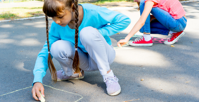 Two kids outside drawing with sidewalk chalk
