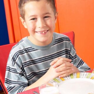 boy sitting at thable with folded hands and a pleasant smile